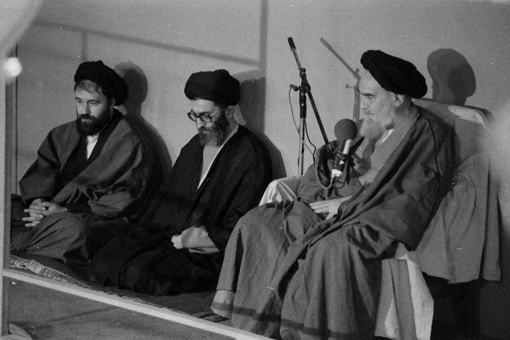 Ruhollah Khomeini, right, oversees the first presidential decree of Ali Khamenei, center, October 9, 1981. (Khamenei.ir, CC BY 4.0)