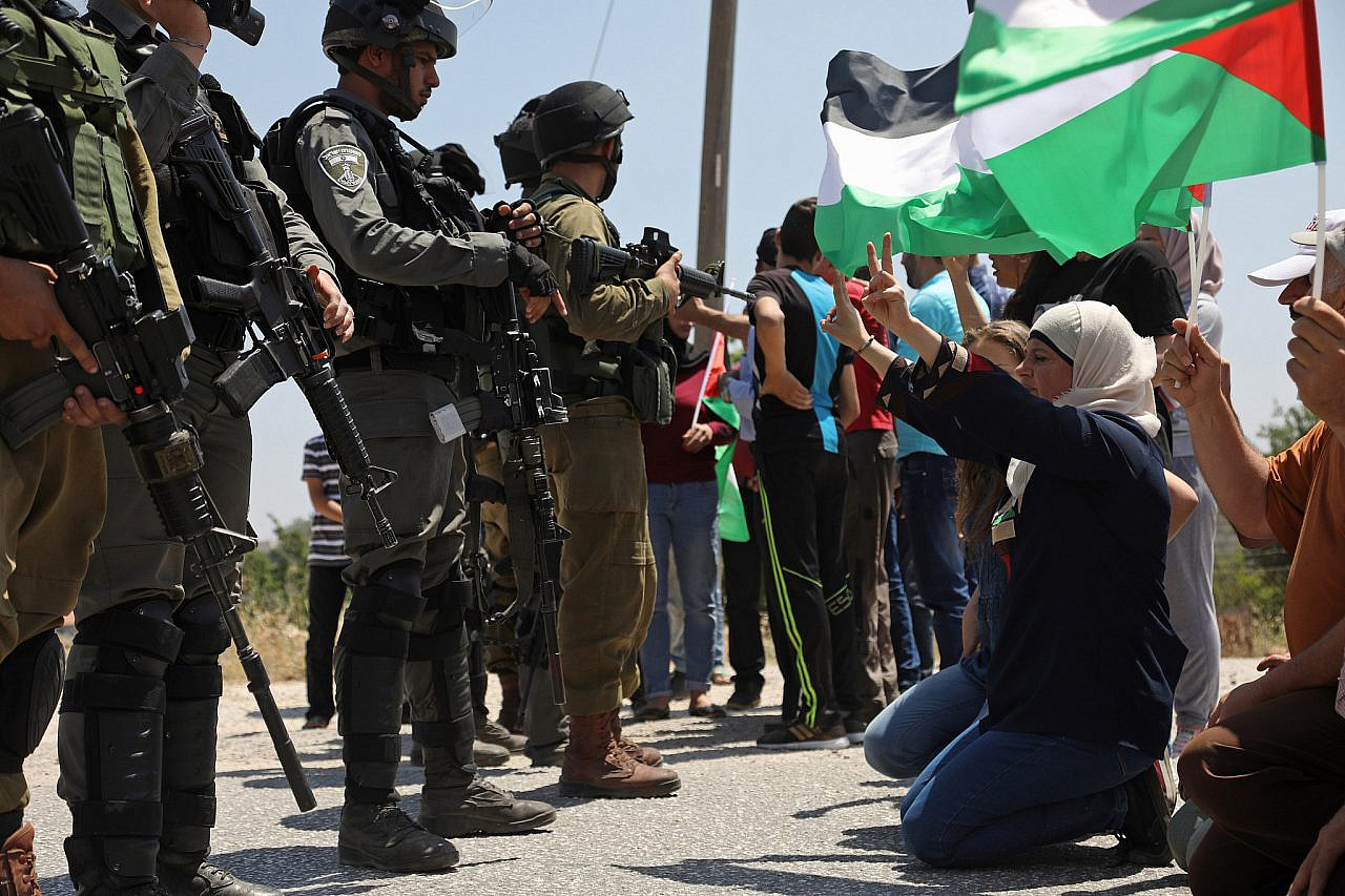 Palestinian protesters sit in front of Israeli soldiers during a demonstration against the occupation, and in solidarity with the Palestinian prisoners' hunger strike, Nabi Saleh, occupied West Bank, May 12, 2017. During the demonstration, Israeli soldiers shot and killed Palestinian youth Saba Abu Ubeid. (Haidi Motola/Activestills)
