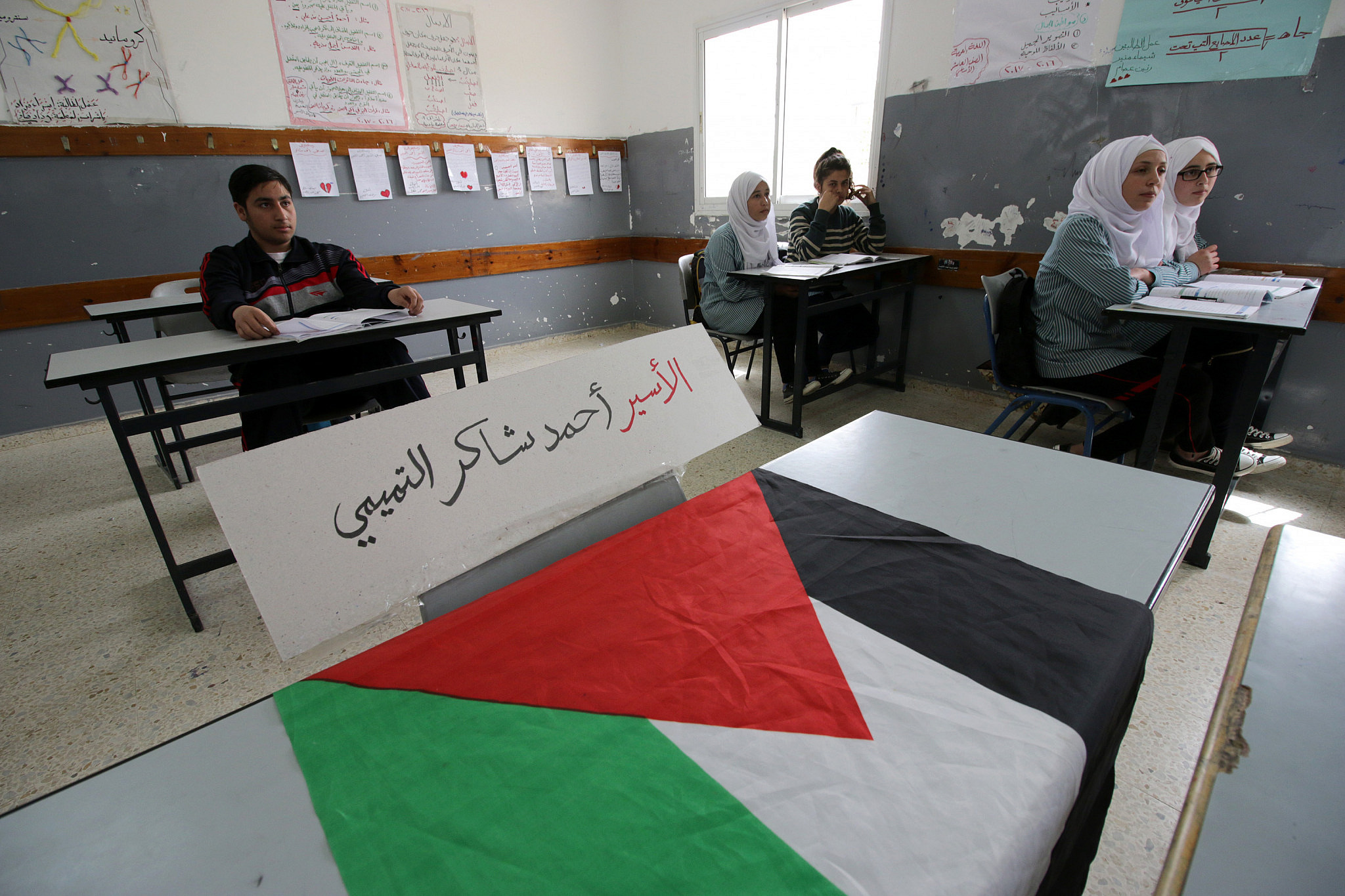 Palestinian students sit in their classroom as a piece of paper that reads "Prisoner Ahmed Tamimi", the name of a 14 year-old student who was arrested by the Israeli army during a night raid two days ago, is placed at his empty seat in the Nabi Saleh elementary school, West Bank, April 26, 2017. (Ahmad Al-Bazz/Activestills)