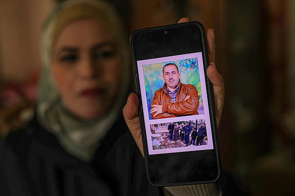 Ola Baqa holds up a photo of her brother who died before she received a permit to leave Gaza and visit him in the West Bank. (Mohammed Zaanoun)