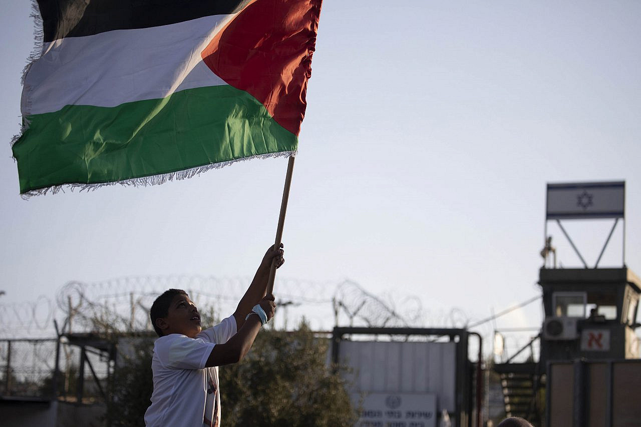 A Palestinian boy waves a fla at a protest outside the Megiddo prison in northern Israel, in solidarity with Palestinian prisoners that were arrested during the events of May 2021 in Lydd/Lod and other cities, August 22, 2021. (Oren Ziv)