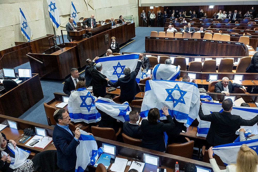 Opposition MKs holding Israeli flags during a discussion and vote on the government's judicial overhaul plans in the assembly hall of the Knesset in Jerusalem, February 20, 2023. (Yonatan Sindel/Flash90)