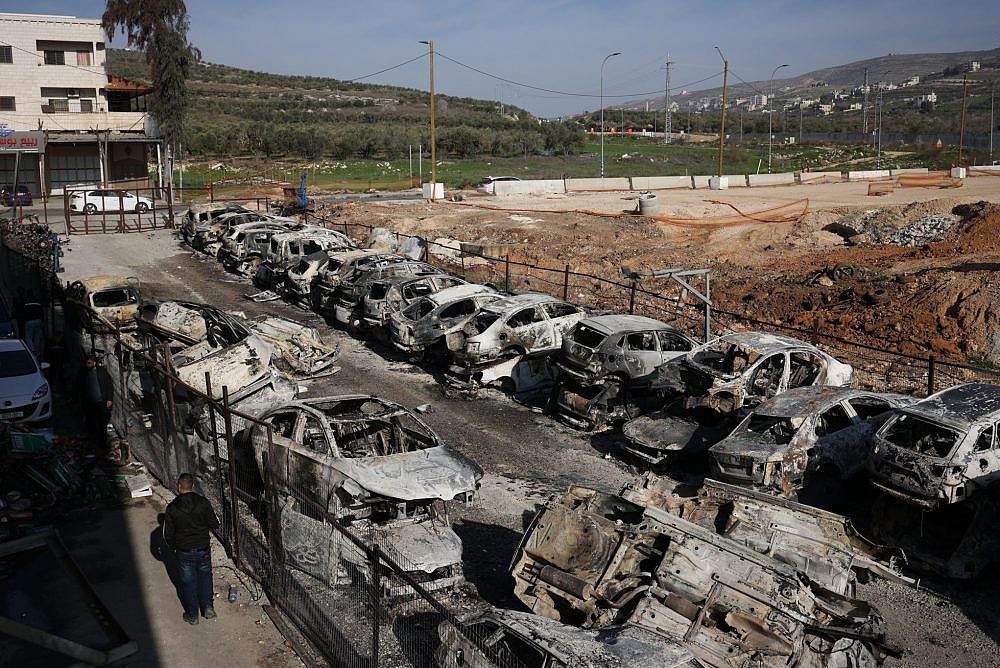 Palestinian residents of Huwara walk among their burned homes, cars, and businesses the morning after Israeli settlers rampaged through their town in the West Bank, Feb. 27, 2023. (Oren Ziv)