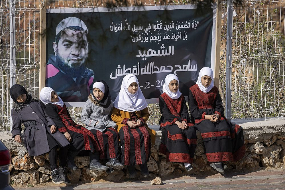 Children in the West Bank village of Za'atra sit in front of a poster commemorating Sameh Aqtesh, who was killed by gunfire during the Huwara pogrom, March 3, 2023. (Oren Ziv)