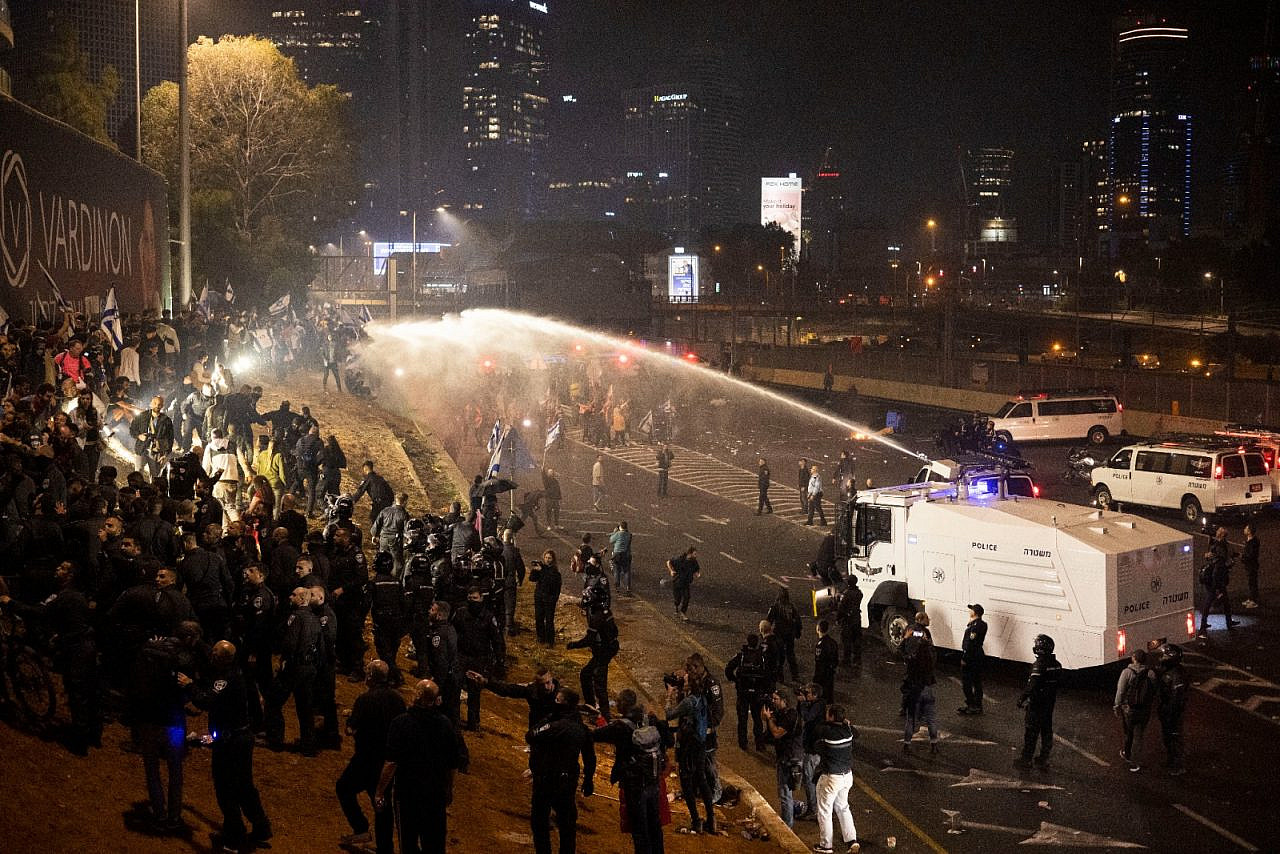 A police water cannon targets protesters on the Ayalon highway, Tel Aviv. Tens of thousands of demonstrators took to the streets following Prime Minister Benjamin Netanyahu's dismissal of Defense Minister Yoav Gallant, after he called to pause the government's planned judicial overhaul, March 26, 2023. (Oren Ziv) 