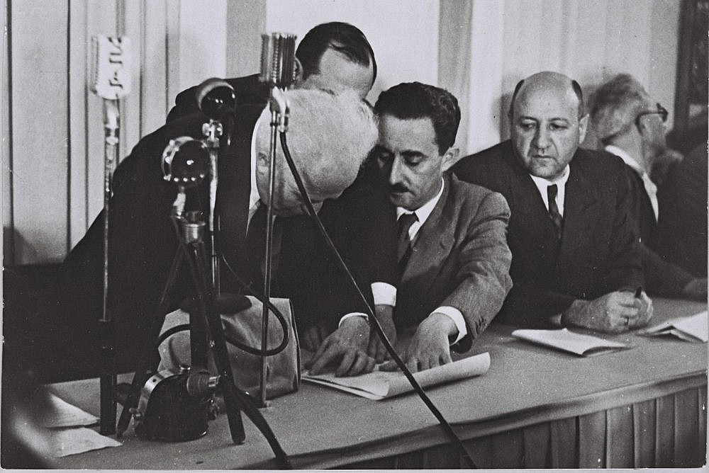 David Ben-Gurion (left) signs the Declaration of Independence held by Moshe Sharett with Eliezer Kaplan looking on at the Tel Aviv museum on Rothschild Boulevard, May 14, 1948. (Israel GPO, PRI OR/CC BY-NC-SA 2.0)