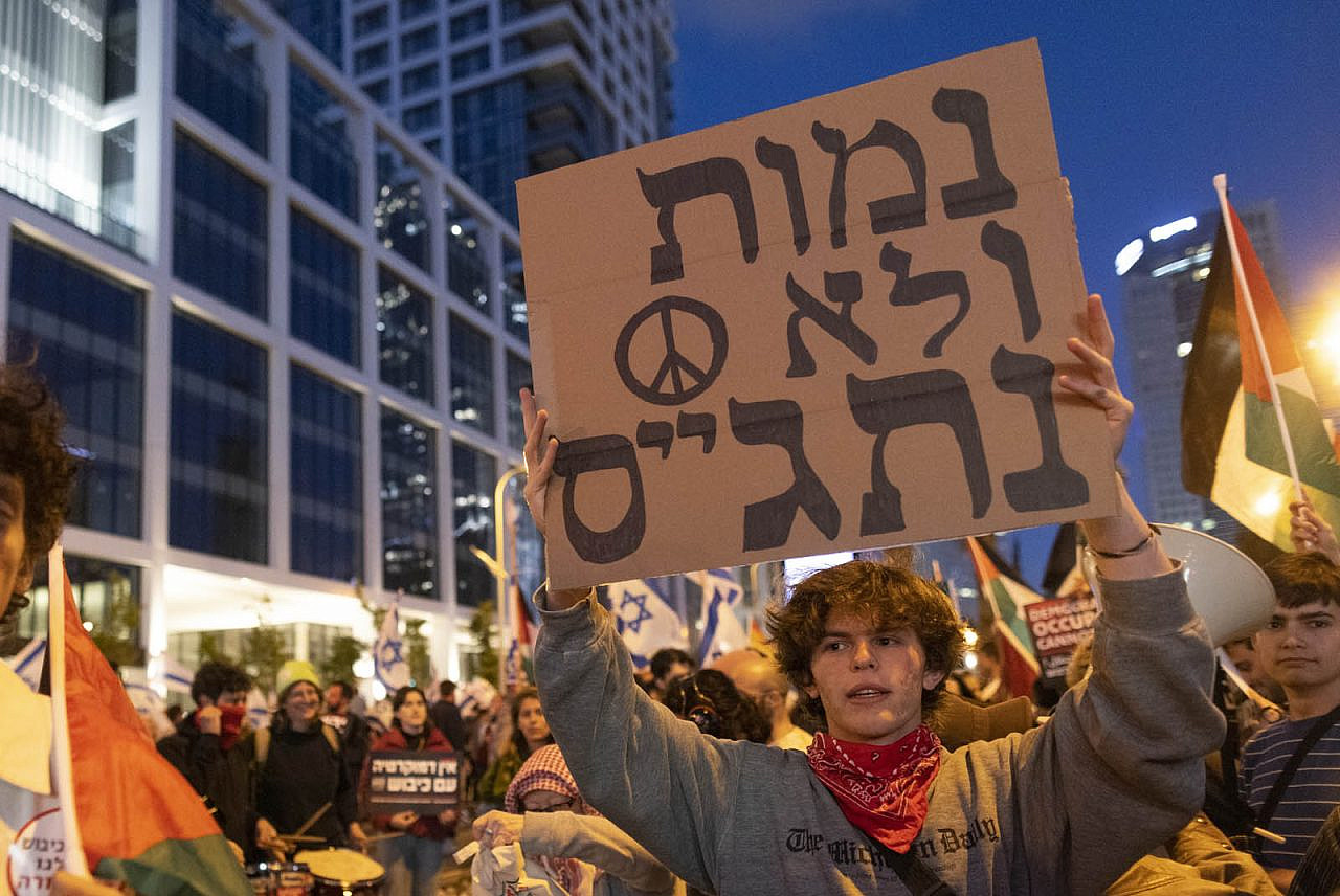 Tal Mitnick holds up a sign that says "We'll die before we enlist" inside the anti-occupation bloc at an anti-government demonstration in Tel Aviv, April 29, 2023. (Oren Ziv)