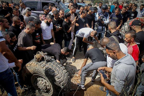Palestinians gather around parts of an Israeli armored vehicle after it was destroyed during clashes between Israeli soldiers and Palestinian fighters in the West Bank city of Jenin, June 19, 2023. (Nasser Ishtayeh/Flash90)