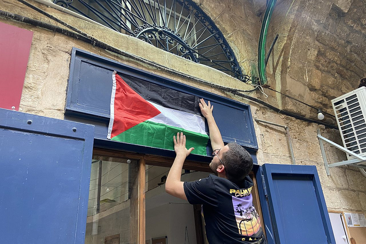 A Baladna youth activist places a Palestinian flag above the entrance to the organization's center. (Maria Zreiq)