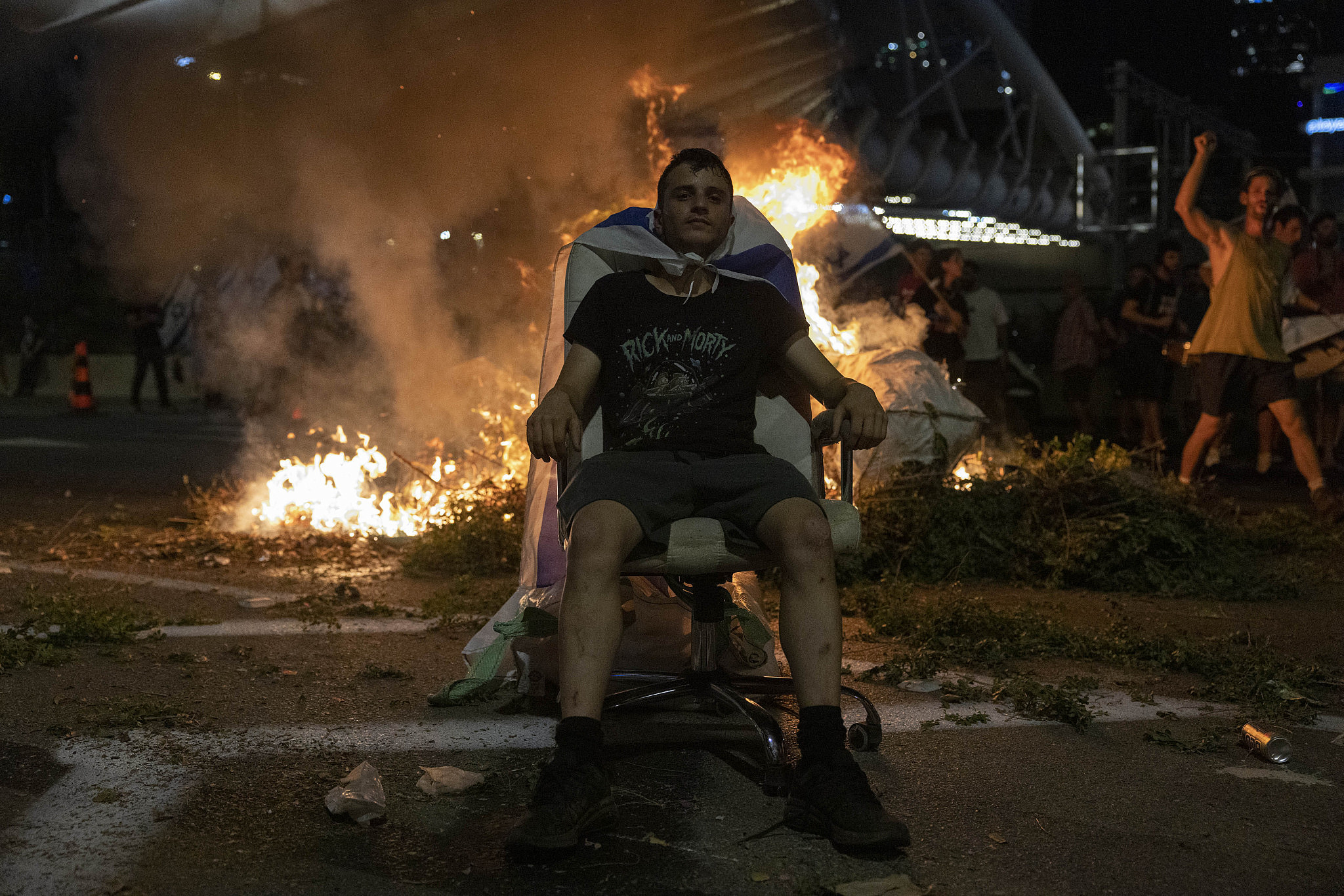 An Israeli protester sits in front of a fire during anti-government protests, Tel Aviv, July 20, 2023. (Oren Ziv)