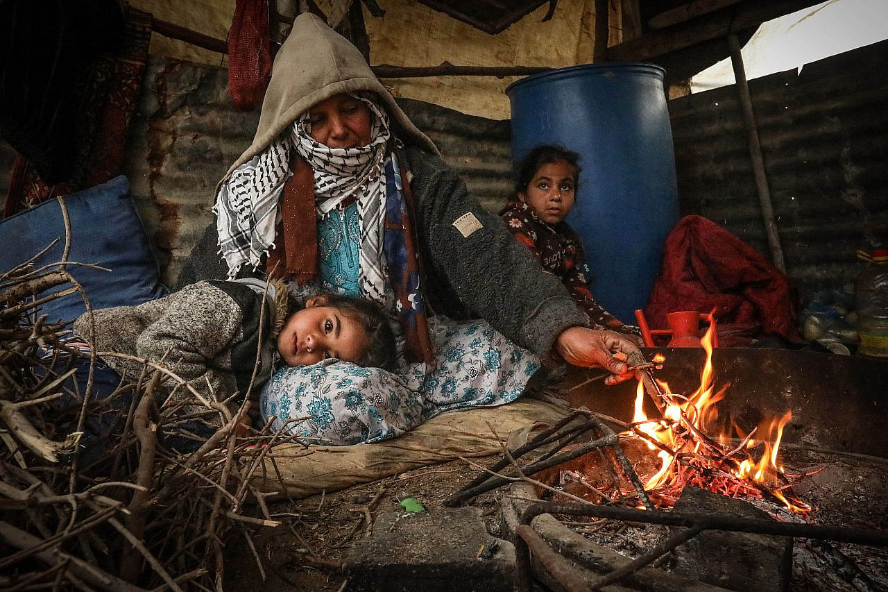 A Palestinian woman and her children sit in a tent as a winter storm approaches the village of Al Mughraqa, south of Gaza city, Gaza Strip, January 7, 2020. (Mohammed Zaanoun/Activestills)