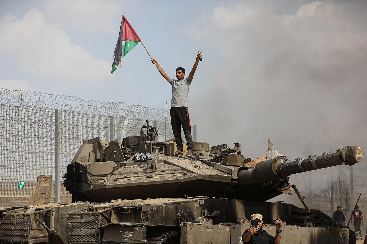 Palestinians stand on top of and beside an Israeli tank inside the border fence with Israel in the city of Khan Younis, southern Gaza Strip, October 7, 2023. (Yousef Mohammed/Flash90)