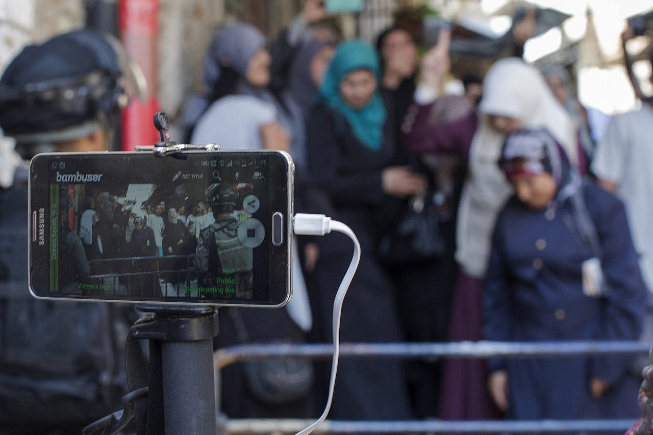 An activist uses a cellphone to live stream as Israeli police forces block Palestinians at an entrance to the Al-Aqsa Mosque compound in Jerusalem's Old City, July 26, 2015. (Faiz Abu Rmeleh/Activestills)