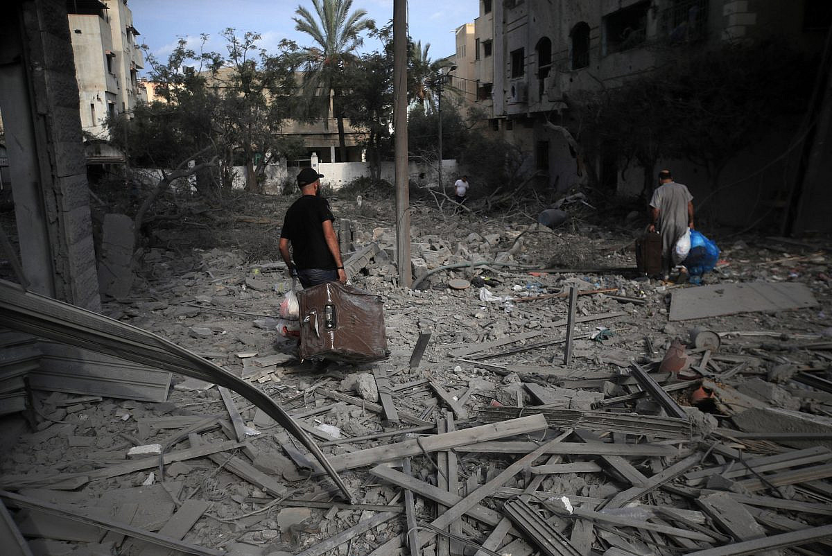 Palestinians carrying luggage walk through the massive destruction caused by Israeli airstrikes in Gaza City's Al-Rimal district, Gaza, October 10, 2023. (Mohammed Zaanoun)