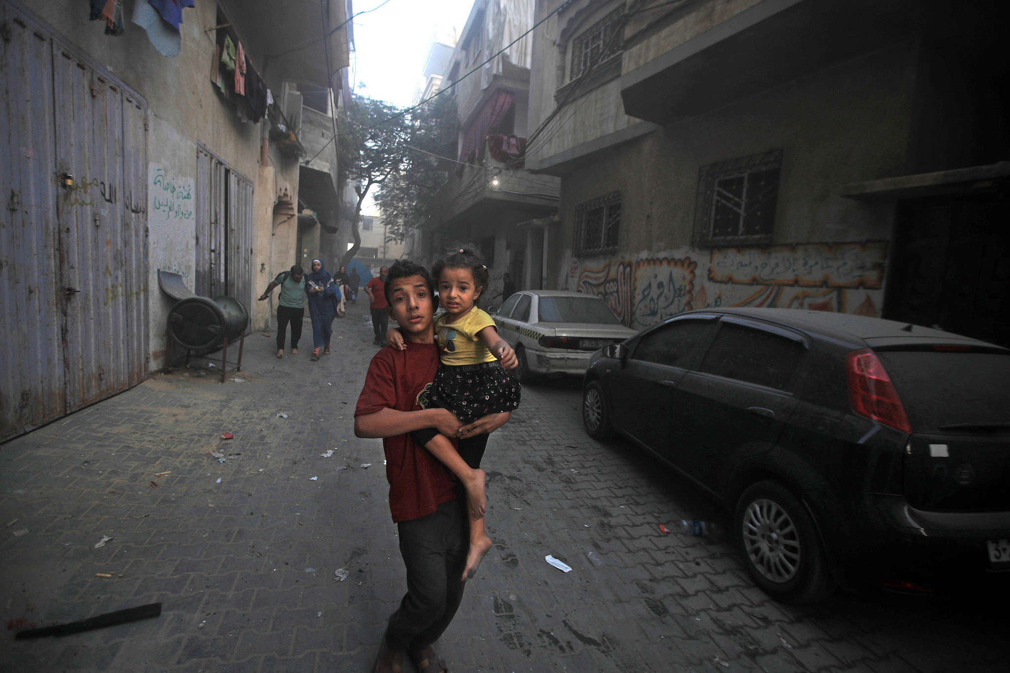 A Palestinian boy carries a young child as they flee an Israeli airstrike on Gaza City, October 11, 2023. (Mohammed Zaanoun/Activestills.org)