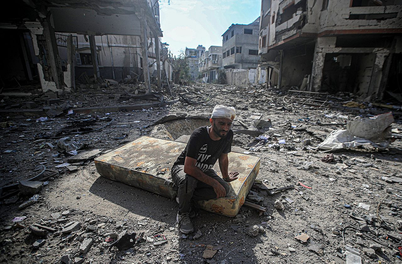 An injured Palestinian sits on a mattress in the Al-Karama neighborhood which was destroyed in Israeli airstrikes, Gaza City, October 11, 2023. (Mohammed Zaanoun)