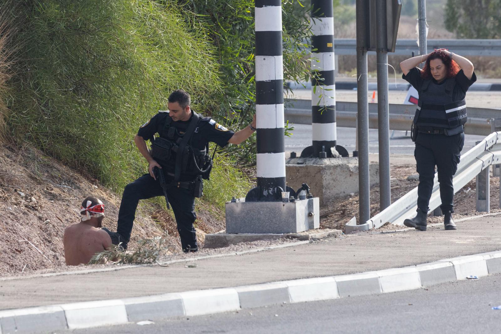 Israeli police officers guard an alleged Hamas militant, on the highway between Ashkelon and Zikim, October 8, 2023. (Oren Ziv)