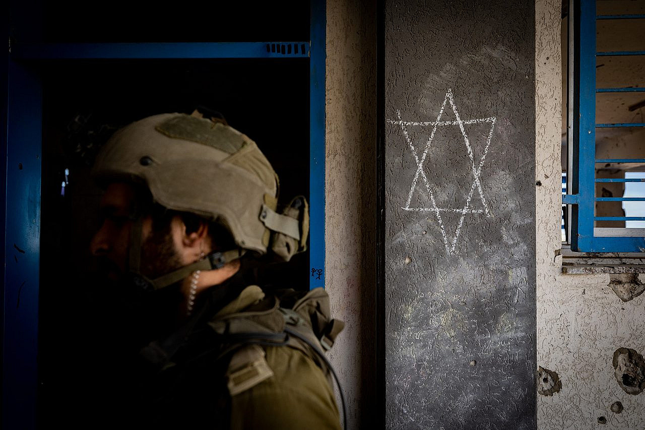 A Star of David is seen behind an Israeli soldier in the Al-Shati refugee camp, northern Gaza Strip, November 16, 2023. (Yonatan Sindel/Flash90)