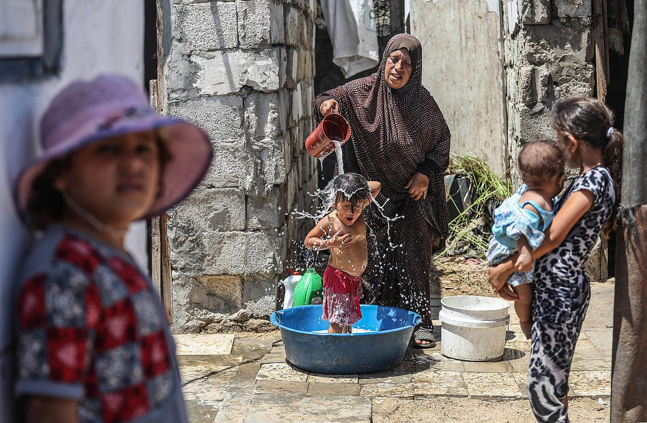 A Palestinian woman washes her child outside their home in Nahr al-Bared refugee camp, Khan Younis, Gaza Strip, August 24, 2019. (Mohammed Zaanoun/Activestills)