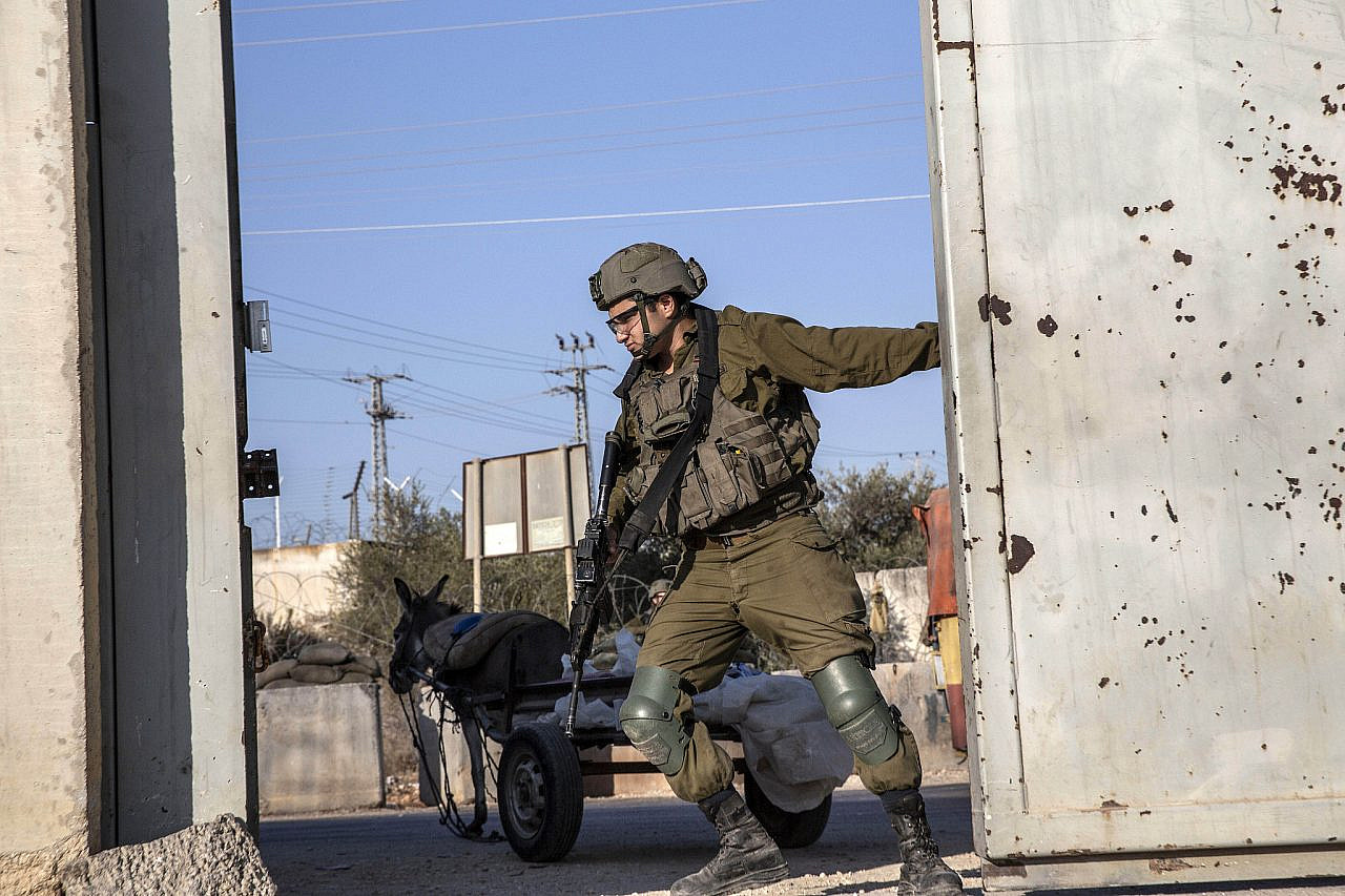 An Israeli soldier closes an agricultural gate in the West Bank wall after Palestinian farmers crossed to access their land during the olive harvest, near the village of 'Azzun 'Atma, occupied West Bank, October 19, 2022. (Anne Paq)