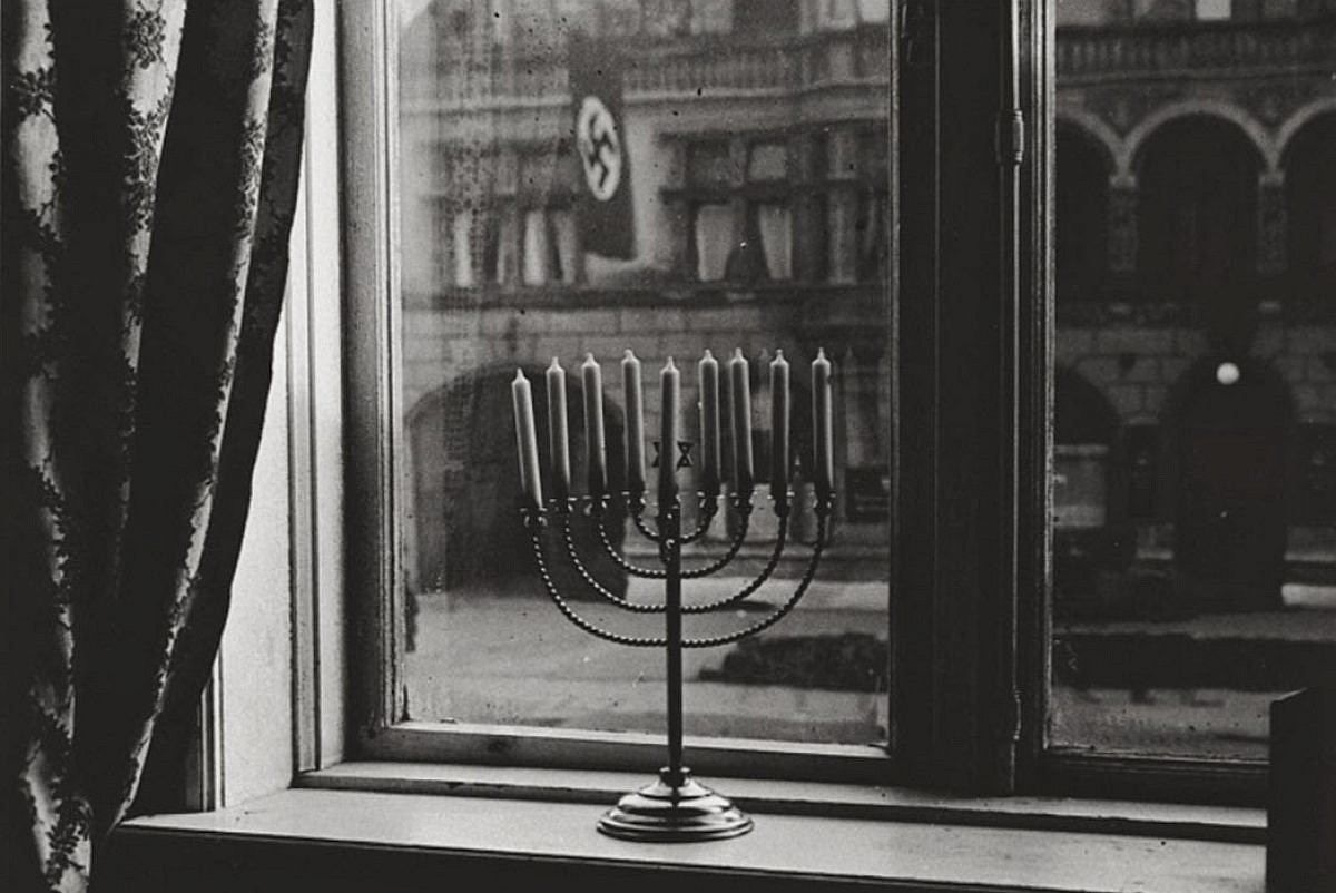 A Hanukkah menorah is seen in a window, with a Nazi flag hanging from a building across the road, Kiel, Germany, 1931. (Courtesy)