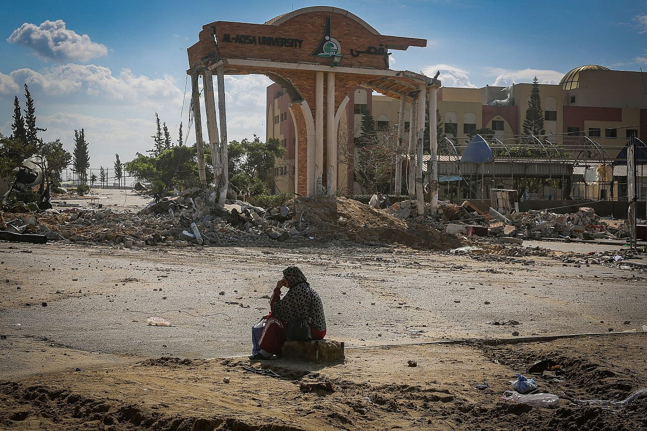 A Palestinian woman sits in front of the damaged entrance to Al-Aqsa University in Khan Younis, southern Gaza Strip, January 26, 2024. (Atia Mohammed/Flash90)