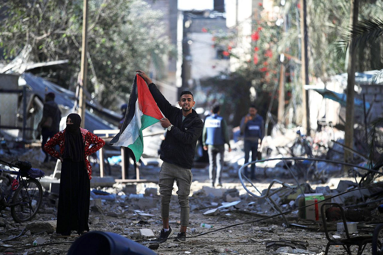 A Palestinian raises his national flag in a destroyed area east of Khan Younis, Gaza Strip, November 24, 2023. (Mohammed Zaanoun/Activestills)