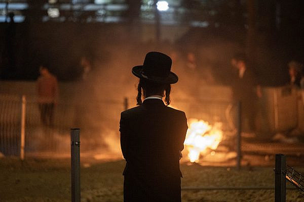A Haredi man watches as a fire burns during a protest against mandatory conscription into the Israeli army, Jerusalem, June 30, 2024. (Oren Ziv)