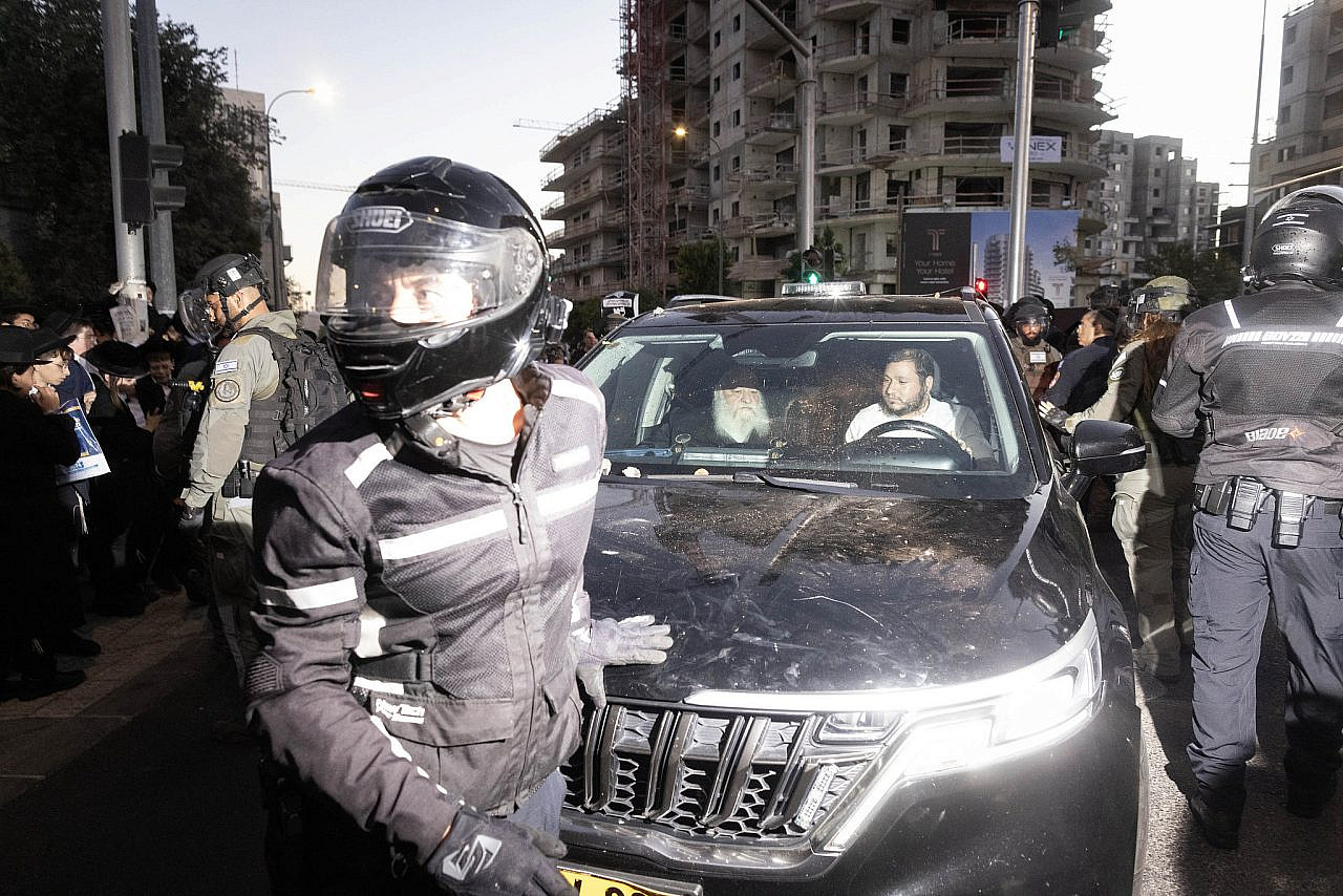 Police protect the car of Housing and Construction Minister Yitzhak Goldknopf as it is attacked during a protest against mandatory conscription into the Israeli army, Jerusalem, June 30, 2024. (Oren Ziv)