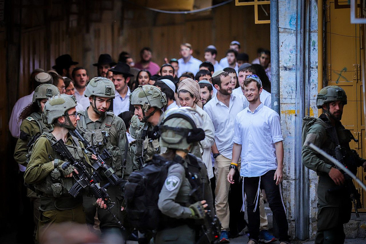 Israeli soldiers stand guard as religious Jews walk through the occupied West Bank city of Hebron, May 25, 2024. (Wisam Hashlamoun/Flash90)