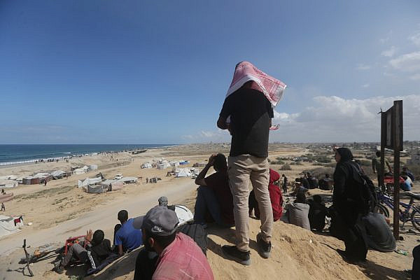 Palestinians watch as other families return from the southern parts of the Gaza Strip to the north, along Al-Rashid Street, October 10, 2025. (Yousef Zaanoun/Activestills)