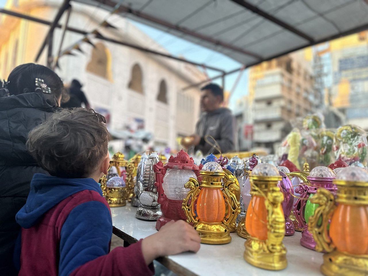 Un bambino allunga la mano verso una fila di lanterne colorate del Ramadan in una bancarella del mercato di Souq Al-Zawiya, nella città di Gaza, 28 febbraio 2025. (Ahmed Dremly)