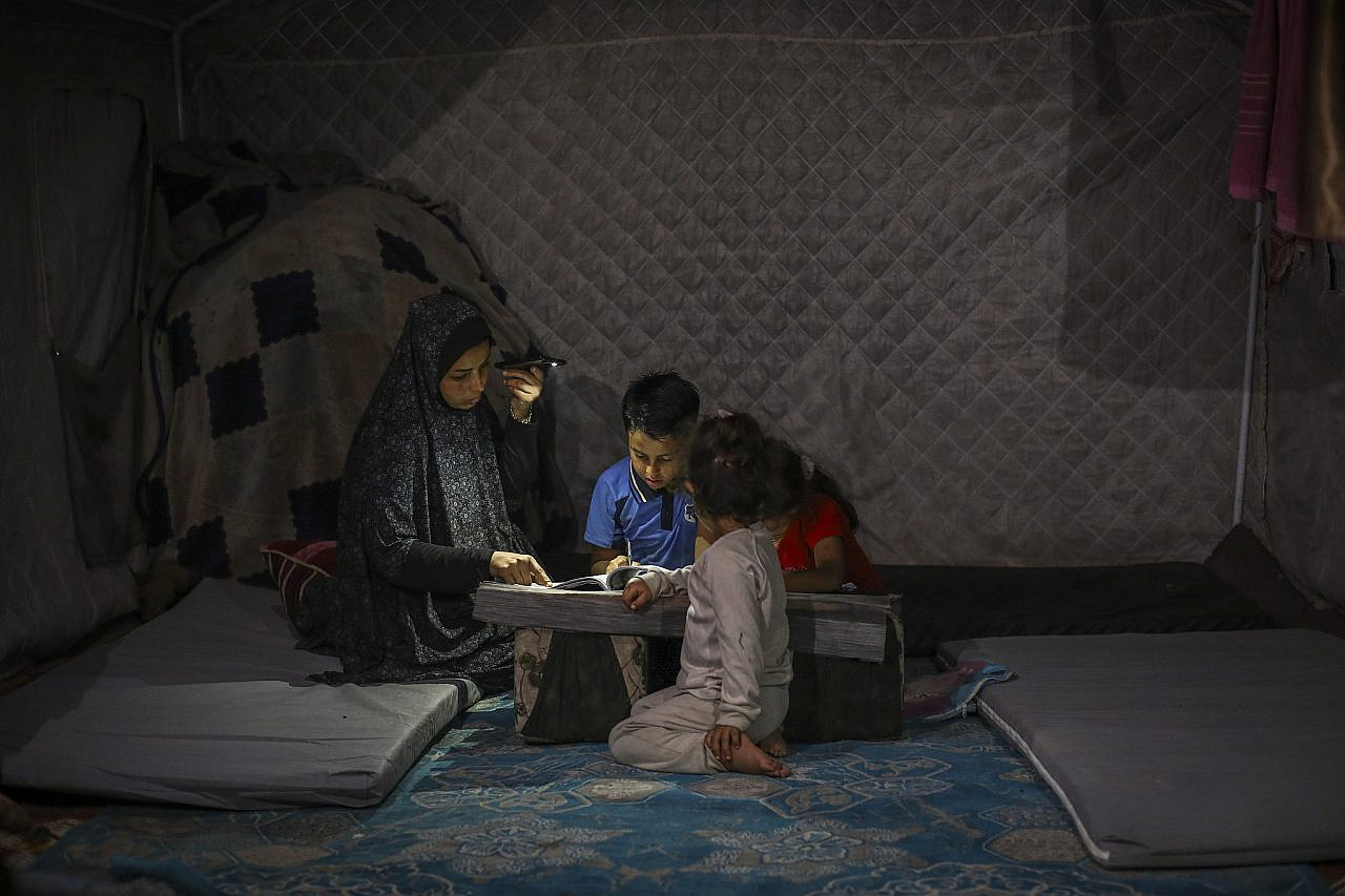 Displaced Palestinian children study by torchlight inside a tent in Gaza City, June 1, 2026. (Ali Hassan/Flash90)