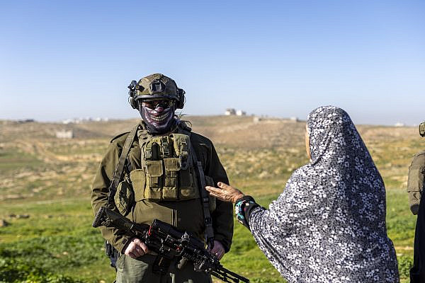 An Israeli soldier ignores a Palestinian woman as he protects a settler grazing cows on agricultural lands belonging to the Palestinian village of Susiya, in Masafer Yatta, January 31, 2026. (Avishay Mohar/Activestills)