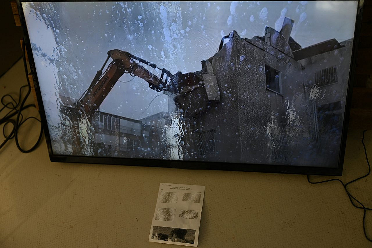 A still from Na'ama Eden Shapira's "The Myth of Clean," showing a bulldozer demolishing old apartment buildings damaged by Iranian missile strikes in Ramat Gan, near Tel Aviv as seen through the windshield of a vehicle passing through a carwash, University of Applied Arts Vienna, July 2026. (Pasha Kogan)