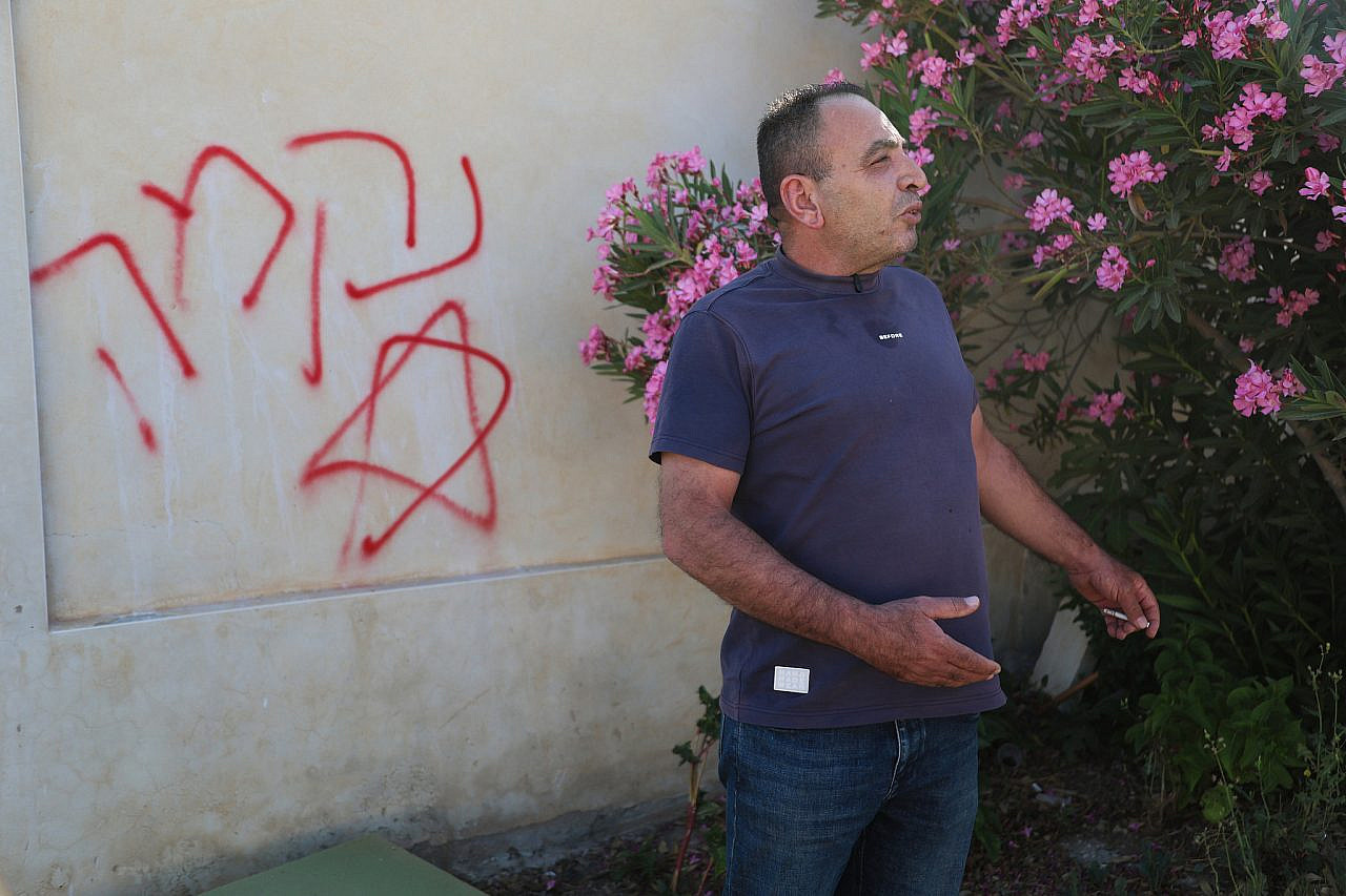A Palestinian man stands next to Hebrew graffiti reading "Revenge" following an attack by Israeli settlers the previous night in the village of At-Tuwani, Masafer Yatta, southern occupied West Bank, July 19, 2026. (Mosab Shawer/Activestills)
