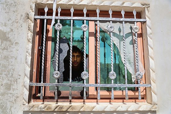 A young Palestinian man looks through the broken window of his house after an attack by Israeli settlers the previous night in the village of At-Tuwani, Masafer Yatta, southern occupied West Bank, July 19, 2026. (Mosab Shawer/Activestills)