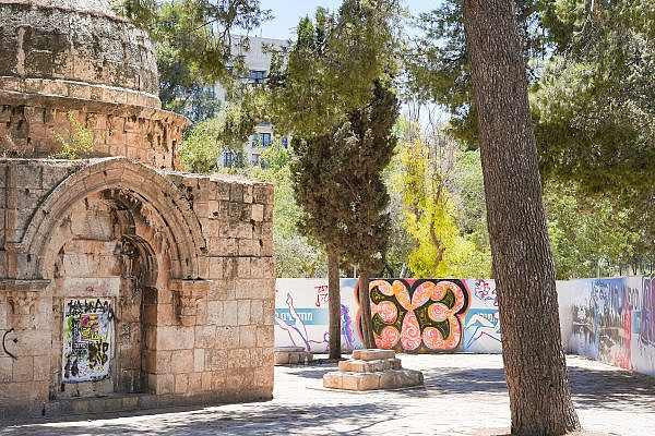 A centuries-old Islamic tomb seen in front of the fence surrounding Mamilla Pool, Mamilla Cemetery, Jerusalem. (Timna Rose Perets)