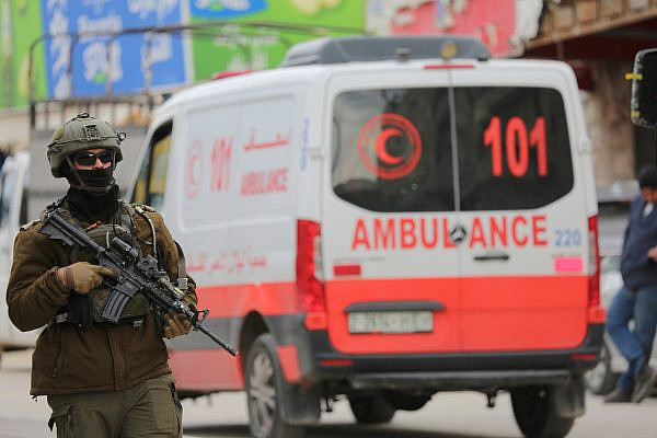 An Israeli soldier stands next to an ambulance after the army curfew was lifted for three hours, in the southern neighborhoods of the West Bank city of Hebron (Al-Khalil), January 21, 2026. (Mosab Shawer/Activestills)