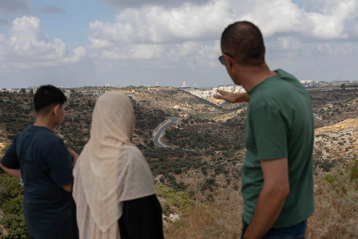 Residents of Bil’in and Kafr Nimah survey the proposed route of the new military road that will run through their lands, with the settlement of Modi'in Illit in the background, Aug. 17, 2026. (Oren Ziv) Residents of Bil’in and Kafr Nimah survey the proposed route of the new military road that will run through their lands, with the settlement of Modi'in Illit in the background, Aug. 17, 2026. (Oren Ziv)
